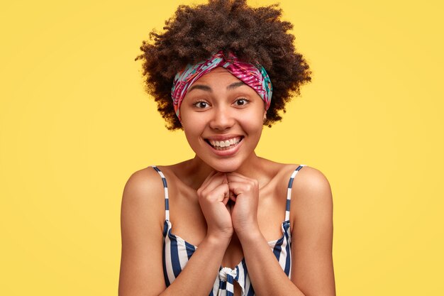 Tête de heureux touché jeune femme afro-américaine sourit doucement, se sent heureux, porte haut rayé et couvre-chef