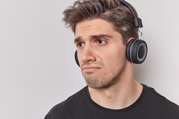 Tête D'un Homme Adulte Brun Mécontent Avec Une Expression Malheureuse Mécontent De La Musique Porte Des écouteurs Stéréo Sans Fil Sur Les Oreilles Regarde Malheureusement Loin Isolé Sur Fond Blanc A Un Jour De Malchance