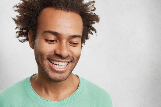 Tête d'homme timide à la peau sombre avec des cheveux croquants, sourit largement, montre des dents blanches, même