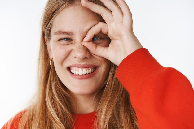 Tête d'une jeune étudiante blonde, charismatique et insouciante, avec des taches de rousseur et des yeux bleus souriant joyeusement faisant un geste correct