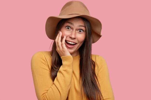 Tête de jeune femme aux taches de rousseur positive avec une expression satisfaite, garde la main sur la joue