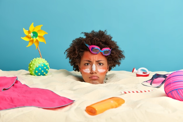 Tête de jeune femme avec crème solaire sur le visage entouré d'accessoires de plage