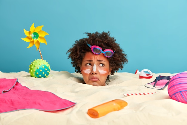 Tête de jeune femme avec crème solaire sur le visage entouré d'accessoires de plage