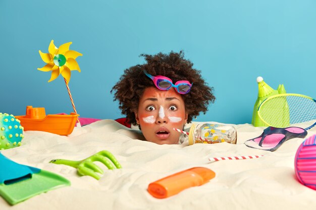 Photo gratuite tête de jeune femme avec crème solaire sur le visage entouré d'accessoires de plage