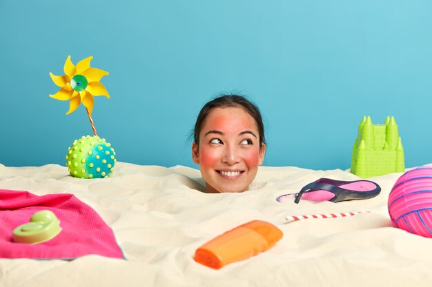 Tête de jeune femme avec crème solaire sur le visage entouré d'accessoires de plage