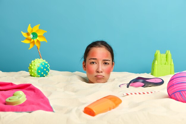Tête de jeune femme avec crème solaire sur le visage entouré d'accessoires de plage