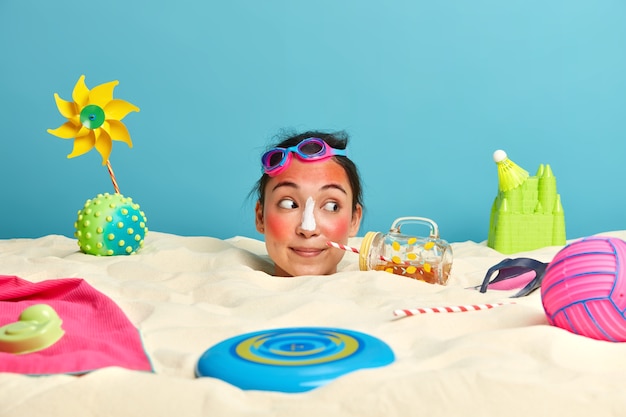 Tête de jeune femme avec crème solaire sur le visage entouré d'accessoires de plage