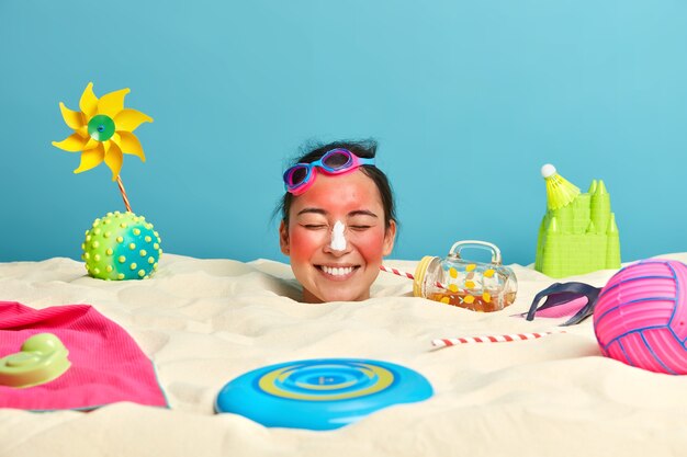 Tête de jeune femme avec crème solaire sur le visage entouré d'accessoires de plage