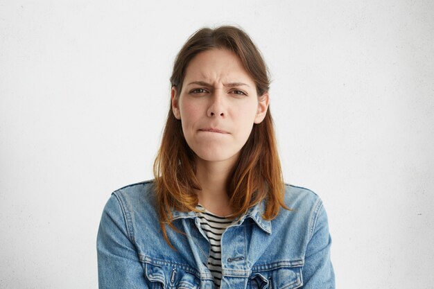 Tête de jeune femme européenne confuse indécise en denim usure des lèvres, son regard exprimant le doute et l'incertitude