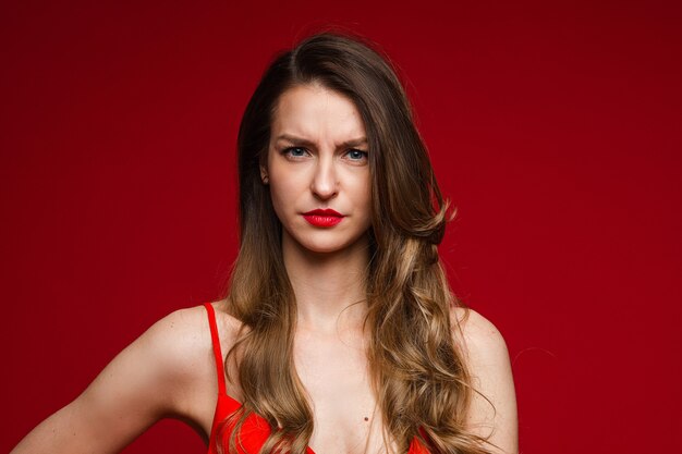 Tête de jeune femme sérieuse mécontente fronçant les sourcils sur fond de studio rouge avec espace de copie pour la publicité