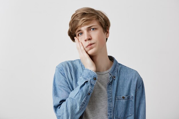 La tête d'un jeune homme bouleversé et stupéfait porte une chemise en jean et garde la main sur la joue, dit: Omg, j'en ai marre. Un homme de race blanche choqué se rend compte de sa faute. Sentiments et émotions négatifs