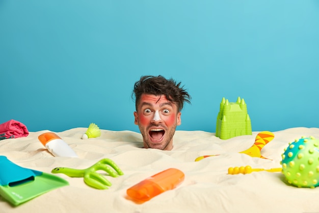 Photo gratuite tête de jeune homme avec crème solaire sur le visage entouré d'accessoires de plage