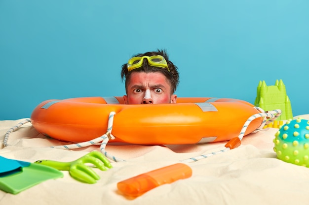 Tête de jeune homme avec crème solaire sur le visage entouré d'accessoires de plage