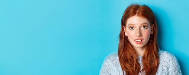 Tête de jolie fille rousse avec des taches de rousseur à la recherche d'espoir et d'innocence devant la caméra debout sur blu