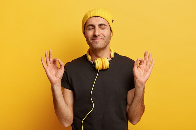 Photo gratuite tête d'un modèle masculin satisfait fait un geste correct avec les deux mains, a les yeux fermés, médite seul à l'intérieur