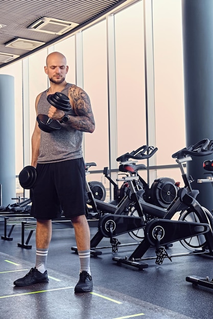 Tête rasée barbu athlétique mâle travaillant avec des haltères dans un club de gym.