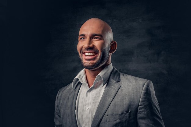 Tête rasée positive masculine vêtue d'un costume gris sur fond gris foncé.