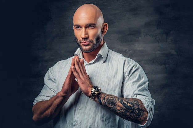 Tête rasée priant mâle avec des tatouages sur son bras.