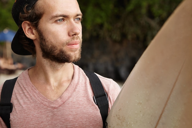 Photo gratuite tête de séduisant jeune homme de race blanche avec expression de visage nostalgique holding paddle board