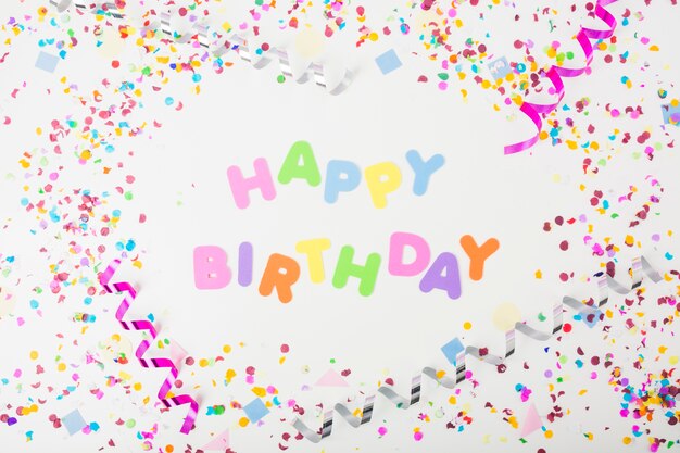 Texte coloré joyeux anniversaire avec des confettis et des banderoles de curling sur fond blanc