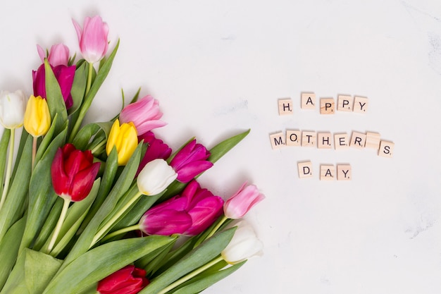 Texte de fête des mères heureux avec des fleurs de tulipes colorées sur fond de béton blanc
