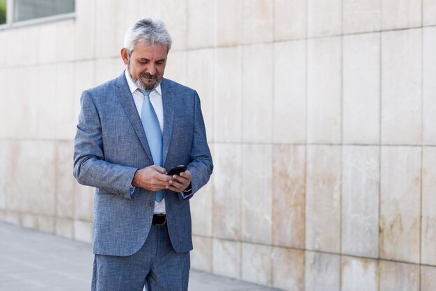 Textes d&#39;affaires senior avec un téléphone intelligent en dehors du bâtiment de bureaux moderne.