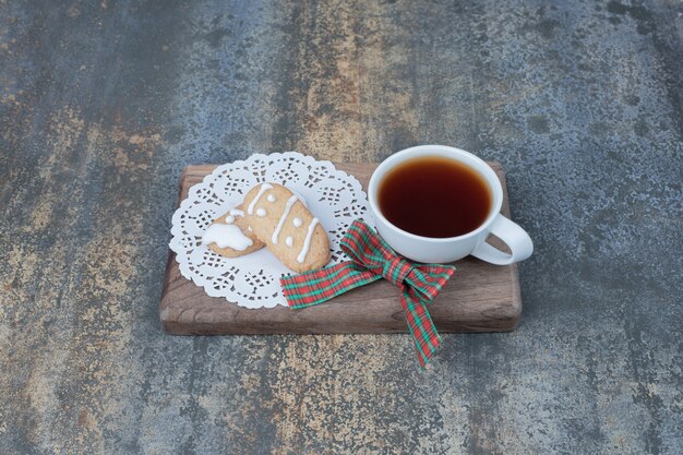 Thé aromatique dans une tasse blanche avec des biscuits de Noël sur planche de bois.