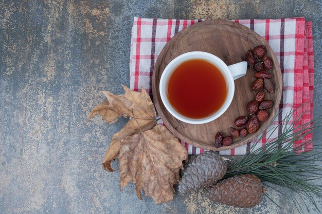 Thé aromatique dans une tasse blanche avec des cynorrhodons et des pommes de pin sur une table en marbre