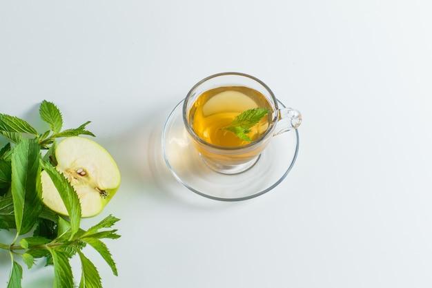 Thé aux herbes, pomme dans une tasse sur fond blanc, pose à plat.