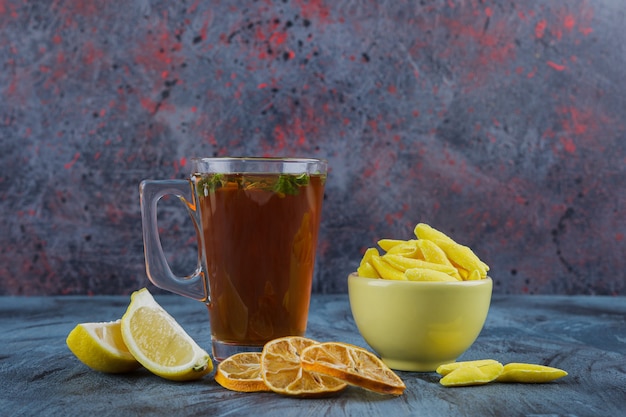 Thé chaud aux citrons et bol jaune de bonbons jaunes sur fond bleu.