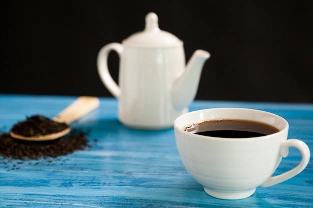 Thé chaud à côté d'une cuillère avec des feuilles de thé sur un tableau bleu vintage sur fond noir