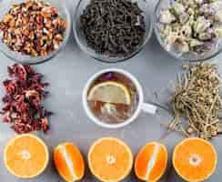 Photo gratuite thé citronné dans une tasse avec des oranges, des herbes à plat sur une surface en plâtre