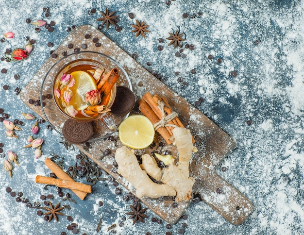 Thé dans une tasse avec farine, choco, biscuits, épices, citron, herbes Vue de dessus sur béton et planche à découper