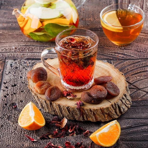 Thé dans une tasse avec des fruits secs, des herbes, de l'eau infusée de fruits, de l'orange et du bois