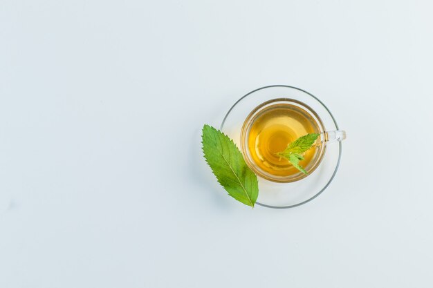 Thé dans une tasse avec des herbes à plat sur un fond blanc