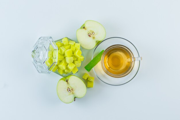 Thé dans une tasse avec pomme, cubes de sucre, bonbons à plat sur un fond blanc