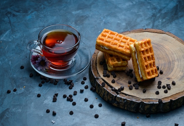 Photo gratuite thé avec gaufre, pépites de chocolat, fleurs dans une tasse sur la surface de la planche bleue et en bois, high angle view.