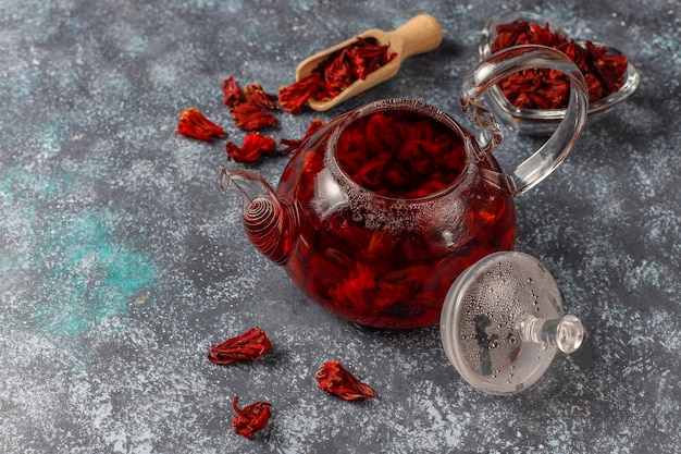 Thé à l'hibiscus chaud dans une tasse en verre et théière en verre.