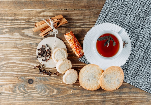 Thé à la menthe avec des bâtons de cannelle, des biscuits, des clous de girofle dans une tasse sur une surface en bois