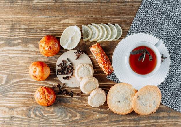 Thé à la menthe dans une tasse de citron en tranches, biscuits, clous de girofle vue de dessus sur table en bois