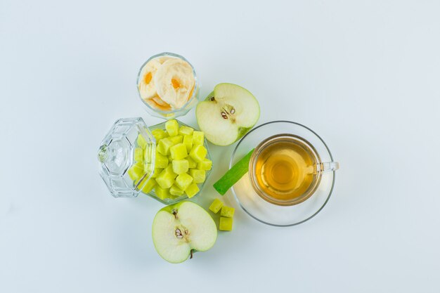 Thé à la pomme, fruits secs, cubes de sucre, bonbons dans une tasse sur fond blanc, pose à plat.