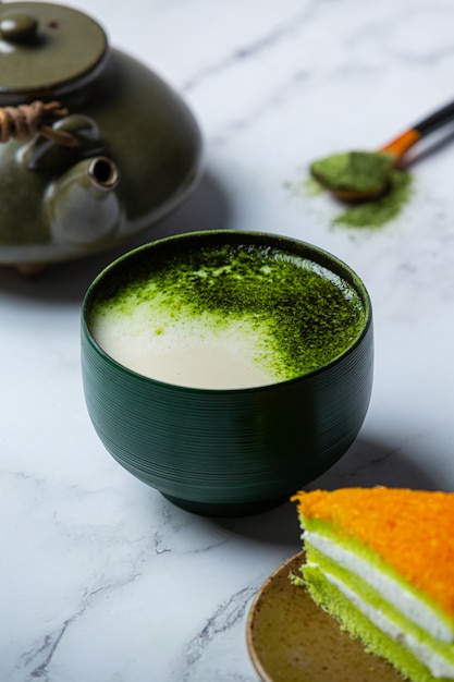 Thé vert chaud dans un verre à la crème garni de thé vert, décoré de poudre de thé vert.