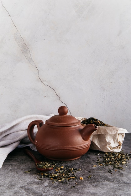 Théière à base de plantes verte avec des feuilles de thé séchées avec une serviette de table contre le mur