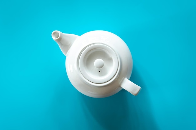 Théière blanche avec thé sur fond bleu à plat