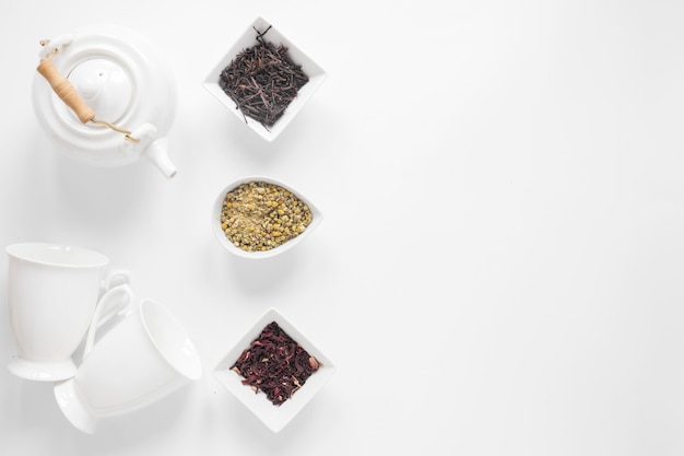 Théière; tasse en céramique; fleurs de chrysanthème chinois séchées; feuilles de thé sèches sur fond blanc