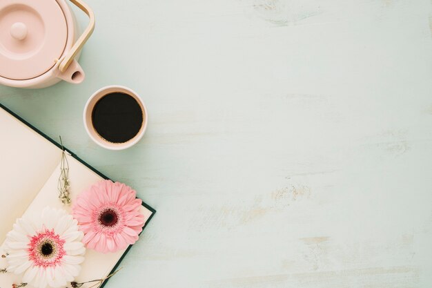 Théière et tasse près de carnet avec des fleurs