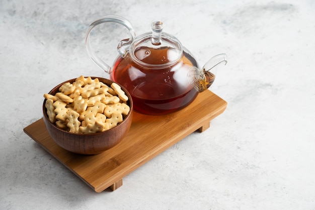 Une théière en verre de thé avec un bol en bois plein de craquelins.
