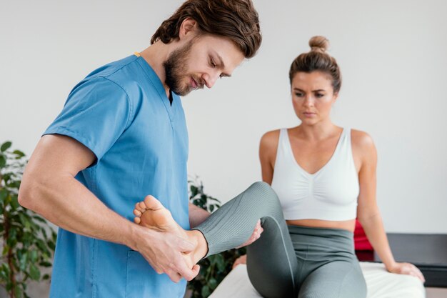 Thérapeute ostéopathe masculin vérifiant le mouvement des jambes de la patiente