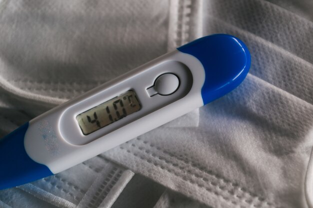 Thermomètre médical indiquant une température élevée sur les masques faciaux-coronavirus