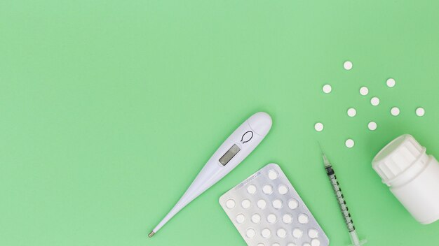 Thermomètre; des pilules; seringue et bouteille en plastique sur fond vert